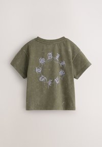 Olivgrön kortärmad t-shirt med rund halsringning. Baksidan pryds av ljusblå text i ett cirkulärt mönster med en strukturerad yta.