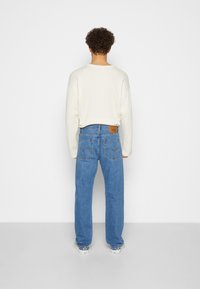 Ljusbeige ribbad tröja med sänkta axlar, ihop med lösa blå jeans med en läderlapp och bakfickor. Vita sneakers.