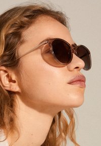 Sunglasses with round, transparent brown frames, dark tinted lenses, and thin temples. Smooth texture and minimalist design.