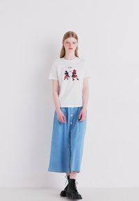 White cotton t-shirt with graphic print featuring characters in black, red, and white. Blue denim skirt with front buttons and a relaxed fit.