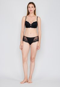 Sort blonde bh med blomsterdesign og vadderede skåle, parret med matchende gennemsigtige sorte trusser med blonder detaljer og en glat finish.