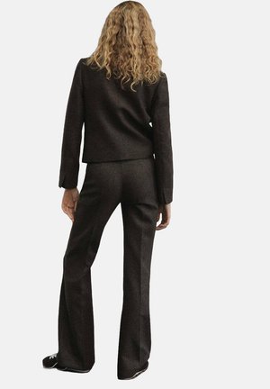 Giacca da suit marrone su misura e pantaloni a zampa d'elefante, realizzati in tessuto testurizzato. Dettagli delle cuciture visibili, silhouette aderente e scarpe da ginnastica nere casual.