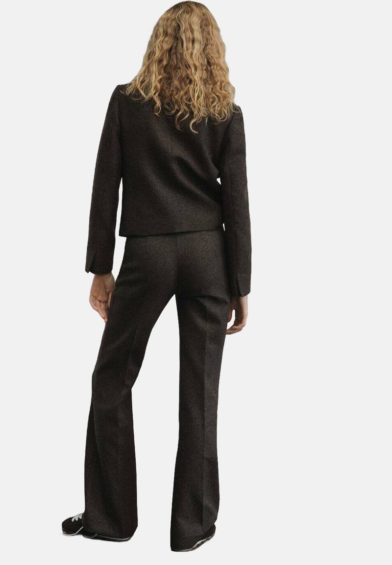 Bruine op maat gemaakte colbert en uitlopende broek, gemaakt van een gestructureerde stof. Zichtbare naden, aansluitende pasvorm en casual zwarte sneakers.