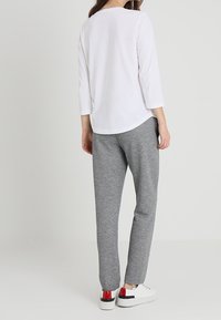 Camicia bianca con maniche a tre quarti abbinata a pantaloni di felpa grigi e sneakers bianche con accenti rossi e neri. Tessuto morbido con una vestibilità rilassata.