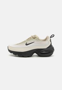 Nike tenisica s zakrivljenim dizajnom u krem i crnoj boji. Izrađene od glatke kože i tkanine, s vidljivom zračnom jedinicom za amortizaciju.