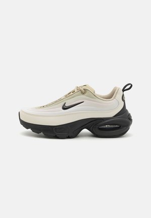 Nike'i spordijalanõud, millel on kõver kuju ja kreemja ning musta värvigammaga. Valmistatud siledast nahast ja kangast, nähtava õhukaitsme unitiga.