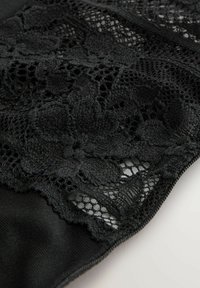 Tissu en dentelle noire avec des motifs floraux, présentant un tissage ouvert complexe et une texture lisse, attaché à un matériau noir uni.