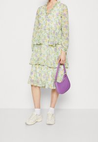 Květnat dress s vrstveným střihem ve světle zelené, žluté a fialové barvě, s volánkovým výstřihem; doplněný fialovou kabelkou a bílými teniskami.