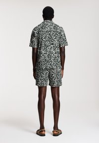T-Shirt mit kurzen Ärmeln und Shorts in Dunkelgrün mit einem weißen abstrakten Muster, aus leichtem Stoff, mit lässigem Schnitt.