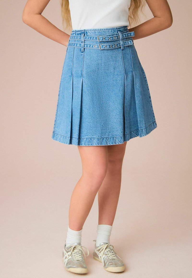 Lichtblauwe denim plooirok met een hoge tailleband, voorzien van dubbele riemen en zilverkleurige accessoires. De textuur is glad met zichtbare stikseldetails.