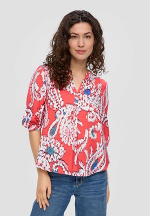 Koraalblouse met een bloemenpatroon in wit en lichtblauw, met een v-hals en mouwen tot de ellebogen, van gestructureerde stof. Gecombineerd met jeans.