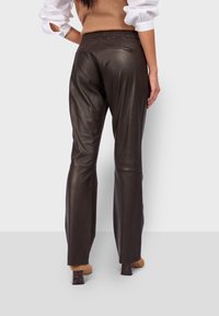 Pantalons en cuir marron au design slim-fit, avec une poche arrière et une texture lisse, associés à des chaussures à talons blocs beiges.