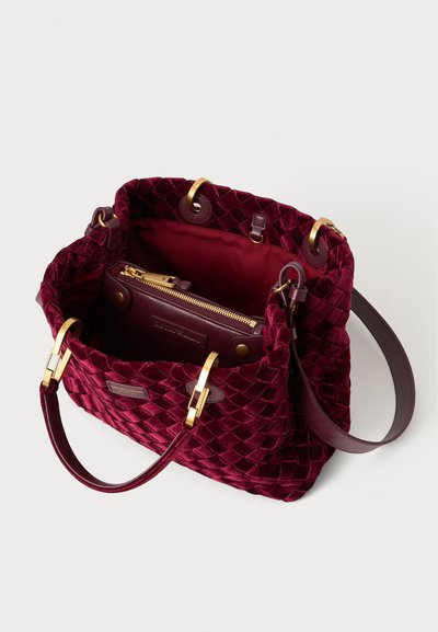 Sac à main en velours rouge profond avec texture matelassée, ferrures dorées, ouverture supérieure montrant une pochette intérieure zippée et des poignées en cuir.