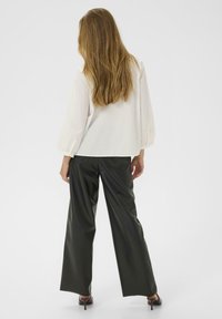 Weiße Bluse mit langen, puffärmeligen Ärmeln, kombiniert mit dunkelgrünen weiten Lederhosen, von hinten präsentiert. Sanfte Stofftextur.