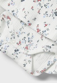 Bodysuit blanc côtelé avec un petit imprimé floral en rouge, bleu et noir. Comprend une fermeture à pression en bas pour faciliter l'habillage.