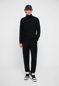 Black turtleneck sweater and matching sweatpants, made of soft fabric. Worn with black and white high-top sneakers and a black cap.