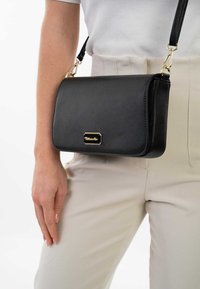 Zwarte rechthoekige handtas van textuurmateriaal met een schouderband. Voorzien van een gouden hardwareaccent aan de voorkant.