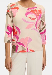 Knitted pullover in light beige with multicolored floral patterns in pink, red, and brown; features a round neck and three-quarter sleeves.