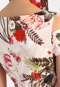 Primo piano della schiena superiore di una persona che indossa un top senza maniche con un motivo floreale colorato che presenta foglie e fiori rossi, bianchi e verdi.