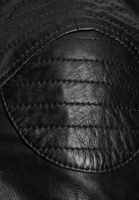 Crna kožna površina s ovalnom ušivenom podstavom koja ima horizontalno šivanje i detaljne šavove.