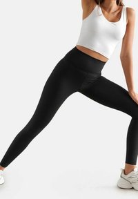Leggings neri a vita alta con un design senza cuciture, caratterizzati da una texture liscia e una vestibilità aderente. Indossati con un top corto bianco.
