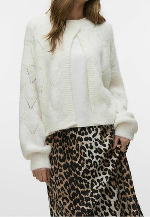 Bílý pletený kardigan s diamantovým vzorem, žebrovanými okraji a balónovými rukávy, nošený přes sukni s leopardím potiskem. Měkká textura.