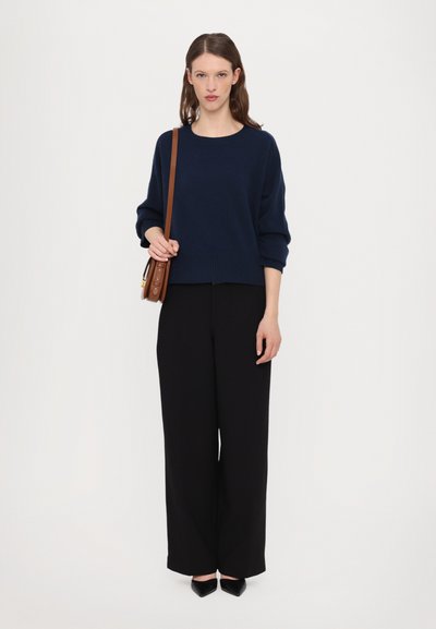 Navy blue knit sweater with a relaxed fit and crew neckline, paired with high-waisted black wide-leg trousers and black pointed-toe shoes.