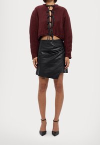 Top in corda di bordeaux tagliato, con dettaglio di lacci sul retro, abbinato a una gonna asimmetrica nera in pelle sintetica e a scarpe col tacco nere.
