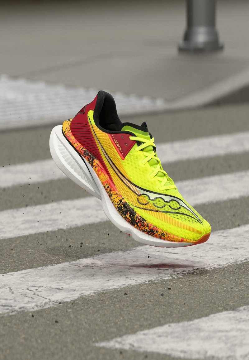 Φωτεινό κίτρινο και κόκκινο αθλητικό παπούτσι με λευκή σόλα στον αέρα πάνω από διάβαση πεζών σε ασφαλτόδρομο, που δείχνει κίνηση και λεπτομέρεια.