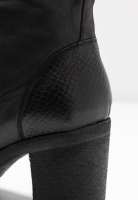 Botín negro de piel con un panel texturizado de patrón de serpiente, tacón bloque alto y acabado suave. Detalle de costura visible en la costura.