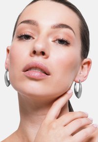 Pendientes de aro de plata con un diseño curvado y alargado. La superficie es lisa y reflectante, con un cierre en la parte superior.