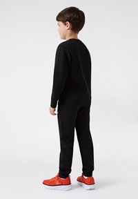 Conjunto de sudadera y pantalones de chándal en negro, material de algodón, diseño sencillo. Destacan unas zapatillas rojas y un logo en la pernera izquierda.