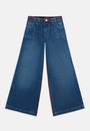 Jeans di jeans blu a gamba larga con vita elastica, bottone frontale e grandi tasche frontali, stesi su uno sfondo bianco.