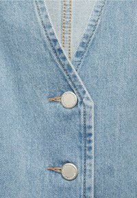 Lyseblå denimjakke med V-hals, kontrastsyninger og to sølvfarvede metalknapper med præget tekst.