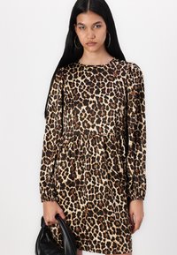 Φόρεμα με λεοπάρ μοτίβο και μακριά μανίκια, με σατεν υφή και  gathered μέση, κρατώντας μία μαύρη τσάντα σε έναν χέρι.