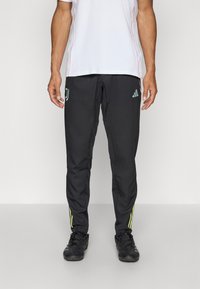 Sorte treningsbukser med Adidas-logo, kontrasterende gule striper ved mansjettene, og teksturert stoff. Sammen med en enkel hvit T-skjorte.