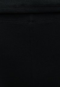 Κοντινή λήψη μαύρου πλεκτού υφάσματος με εμφανές κάθετο ραφή και λεπτομέρεια ραφής κοντά στην πάνω άκρη.