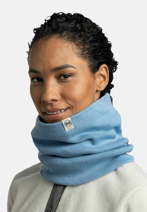 Blue neck warmer made of soft fabric features a circular design with a logo tag visible at the top. Worn over a light-colored jacket.