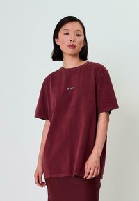 Vínová oversized tričko s krátkým rukávem, s bílým textem "OH APRIL" na hrudi. Měkký materiál a volný střih.