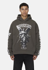 Hoodie vert olive arborant un graphique central d'une figure ailée tenant une épée. Texte "GOOD FOR NOTHING" en gras blanc, manches longues avec des accents blancs.