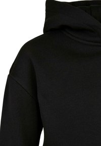 Felpa nera con un tessuto morbido e strutturato. Presenta un colletto alto e una vestibilità comoda, caratterizzandosi per un design pulito e minimalista.