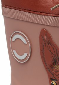 Kumisaappaat, joissa on vaaleanpunainen runko, ruskea yläosa, kohokuvioitu logo ja painettu eläinkuvio, jossa on ruskeaa turkkia ja keltaisia yksityiskohtia. Teksturoitu pohja paremman pidon saavuttamiseksi.