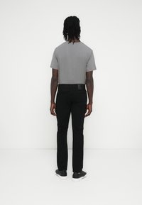 Γκρι κοντομάνικη μπλούζα, μαύρο τζιν στενής εφαρμογής και μαύρα αθλητικά παπούτσια. Απλός σχεδιασμός με λείο ύφασμα, απεικονιζόμενο από την πίσω πλευρά.