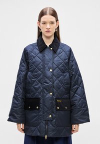 Tengerészkék steppelt dzseki fekete kordbársony gallérral, arany színű részletekkel, két elülső zsebbel és cipzáras rögzítéssel a további részletekért.