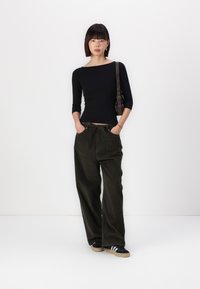Zwarte top met lange mouwen; donkergroene, wijde corduroy broek met een trekkoord; zwarte sneakers met witte strepen; bruine schoudertas.
