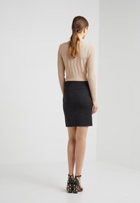 Pull cropped beige à côtes avec motif en losanges, associé à une jupe noire ajustée et des sandales à talons hauts noires ornées de clous dorés.