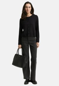 Zwarte cardigan met knopen, gecombineerd met donkergrijze flared jeans. De outfit wordt aangevuld met een zwarte leren tote bag en zwarte laarzen.