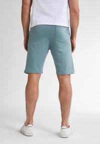 Lichtblauwe katoenen shorts met een rechte snit, elastische tailleband en een achterzak. Gecombineerd met witte sneakers met groene accenten.