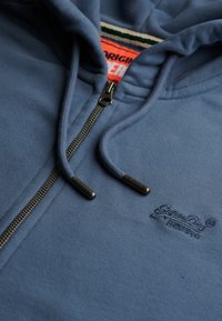 Felpa con cappuccio blu con zip, realizzata in tessuto morbido, con zip a contrasto, logo ricamato e coulisse con punte metalliche.