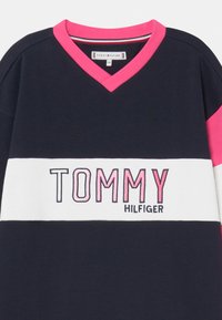 Námořnická bavlněná mikina s růžovými akcenty, bílým horizontálním pruhem a vyšívaným logem "TOMMY HILFIGER". Návrh s véčkovým výstřihem.